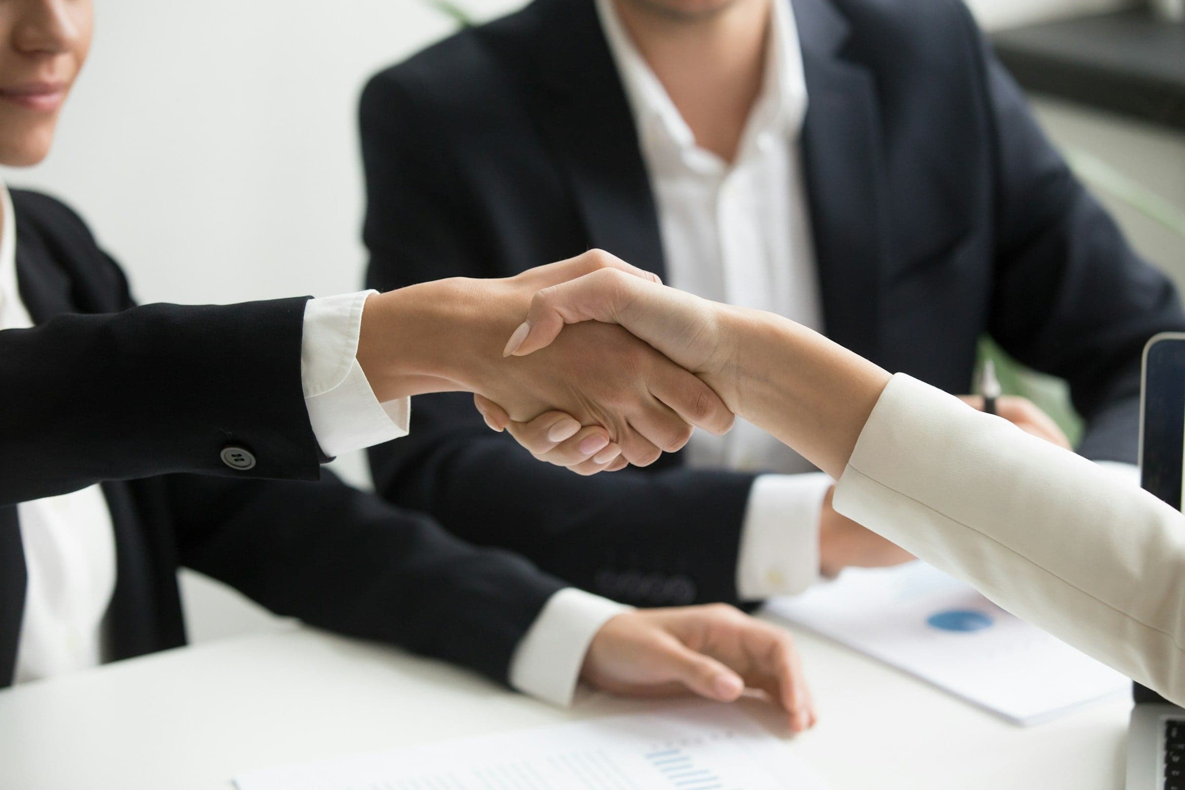 Two professionals shaking hands across a desk: the moment a handoff is accepted and a sealed sign-off records it.